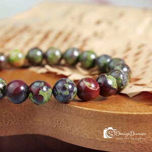 Close-up of dragon blood stone beads, showcasing the intricate patterns of deep green scales interwoven with vibrant red spots.