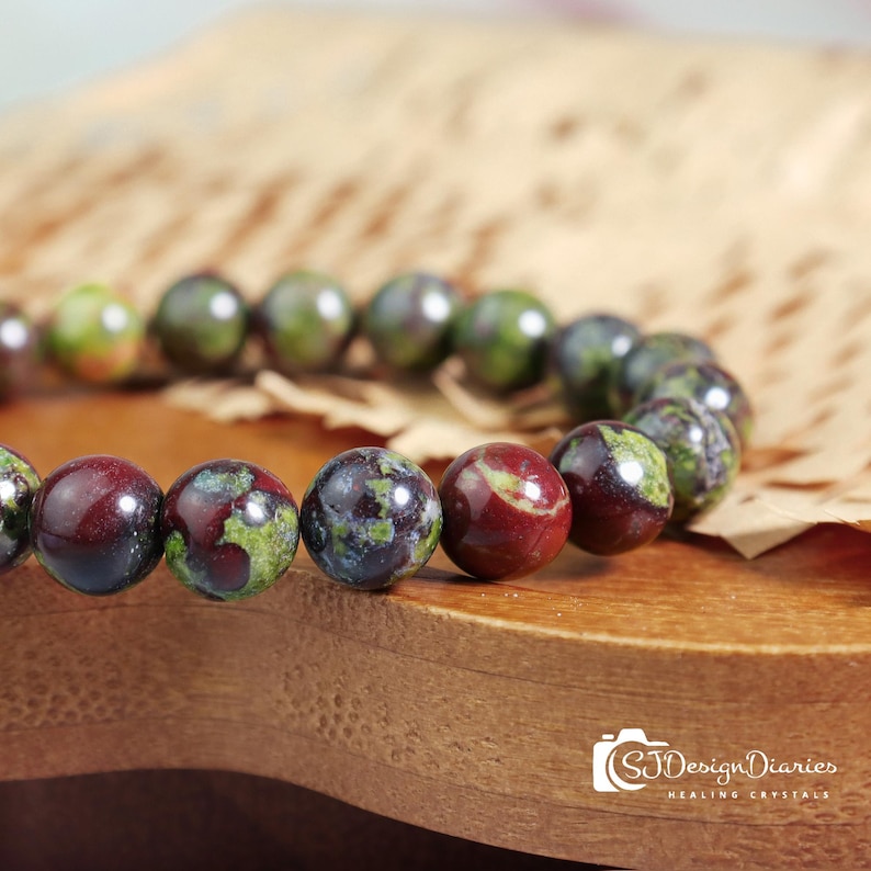 Close-up of dragon blood stone beads, showcasing the intricate patterns of deep green scales interwoven with vibrant red spots.