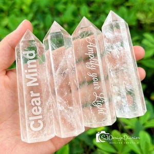 Può includere: Quattro punte di cristallo di quarzo trasparente con testo inciso. Due cristalli recitano "Clear Mind" e "Amplify your Light". I cristalli sono tenuti in mano su uno sfondo verde sfocato. Sono cristalli curativi.