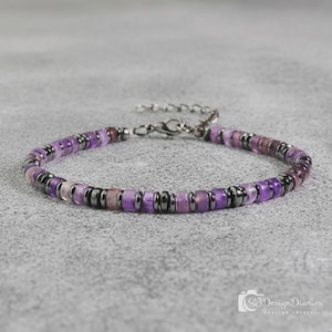 May include: A beaded bracelet featuring alternating cylindrical purple amethyst beads and small, dark metallic hematite spacer beads. The bracelet includes a silver-toned metal lobster claw clasp and a short extender chain for adjustable sizing.