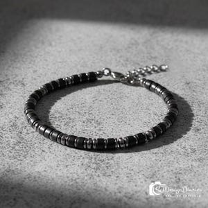 May include: A bracelet featuring alternating matte black cylindrical beads and polished metallic silver-tone spacer beads. The piece includes a silver-tone metal lobster claw clasp and an adjustable extender chain with small circular links.