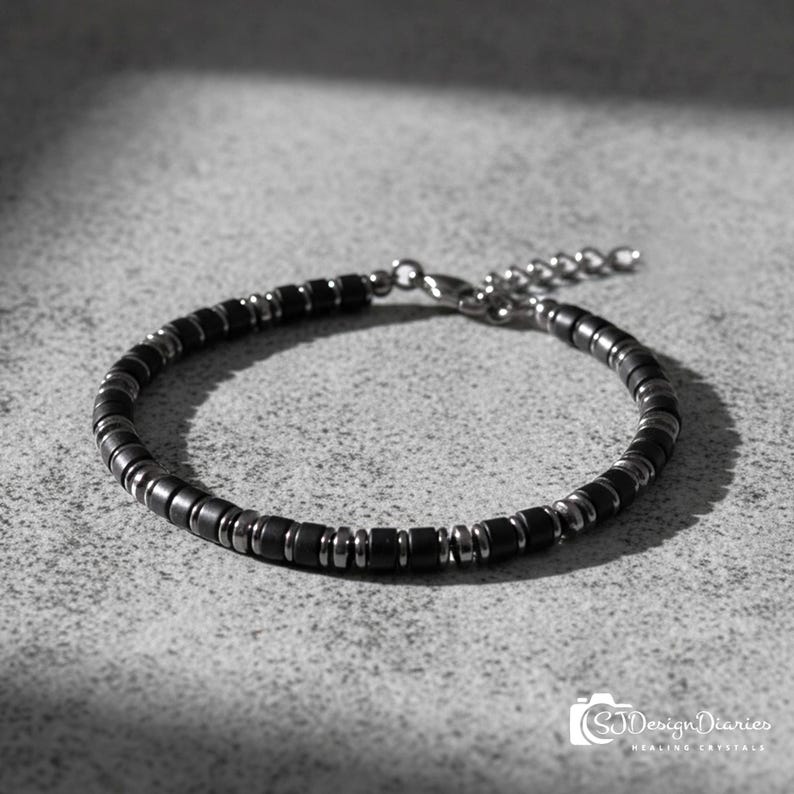 May include: A bracelet featuring alternating matte black cylindrical beads and polished metallic silver-tone spacer beads. The piece includes a silver-tone metal lobster claw clasp and an adjustable extender chain with small circular links.