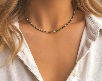 May include: A delicate choker necklace featuring a single strand of small, round, metallic pyrite beads with a reflective, dark gold finish. The beads are uniform in size and strung closely together to form a continuous, shimmering circular band.