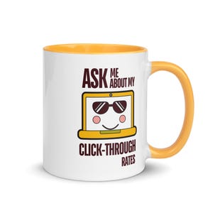 May include: White ceramic mug with a yellow interior and handle. The mug features a cartoon laptop design wearing sunglasses, with the text "ASK ME ABOUT MY CLICK-THROUGH RATES" in brown lettering. A fun and quirky design.