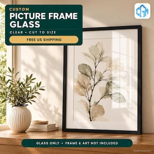 May include: Custom picture frame glass, clear and cut to size. The image features a black rectangular frame containing a botanical print of leaves in muted green and beige tones, displayed next to a white ribbed ceramic vase.