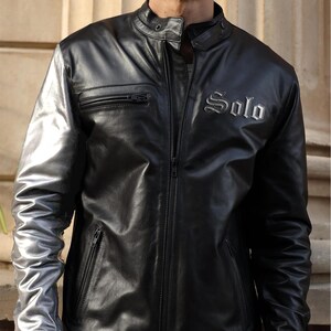 May include: Black leather jacket with silver sleeves and the word "Solo" embroidered on the chest. The jacket features a zippered front, a small zipped pocket, and a stand-up collar. The sleeves are a metallic silver colour.