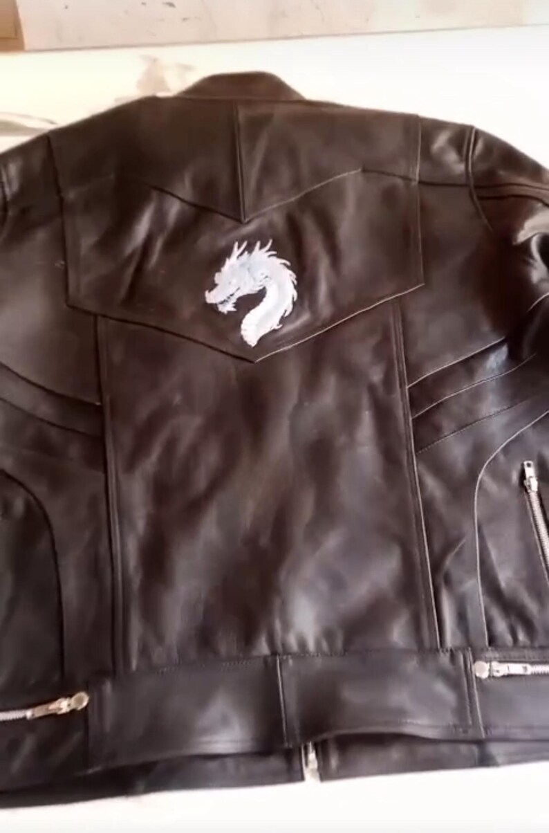 May include: A black leather jacket featuring a white dragon emblem on the back. The jacket has a classic biker design with zip closures and a tailored fit. The leather appears smooth, and the stitching is visible.