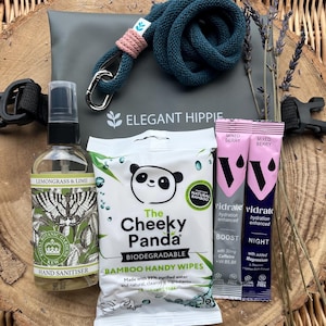 May include: A selection of self-care products, including hand sanitiser, bamboo wipes, and hydration sachets, displayed on a wooden surface. The items feature branding such as "Elegant Hippie" and "The Cheeky Panda". A teal rope lanyard with a pink detail is also present.