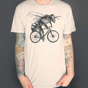 Peut inclure: Un t-shirt beige avec une illustration en noir et blanc d'une abeille à vélo.