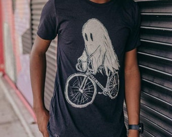 May include: A black t-shirt with a white graphic of a ghost riding a bicycle. The ghost has two eyes and a smile. The bicycle has the words "Ghost Cycle" written on the frame.