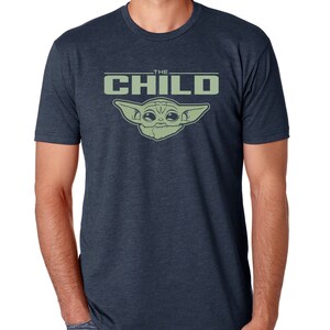 May include: Navy blue t-shirt featuring a green graphic of "The Child" from the Star Wars series. The text "THE CHILD" is above the character's image. The shirt is short-sleeved and made of a soft material.