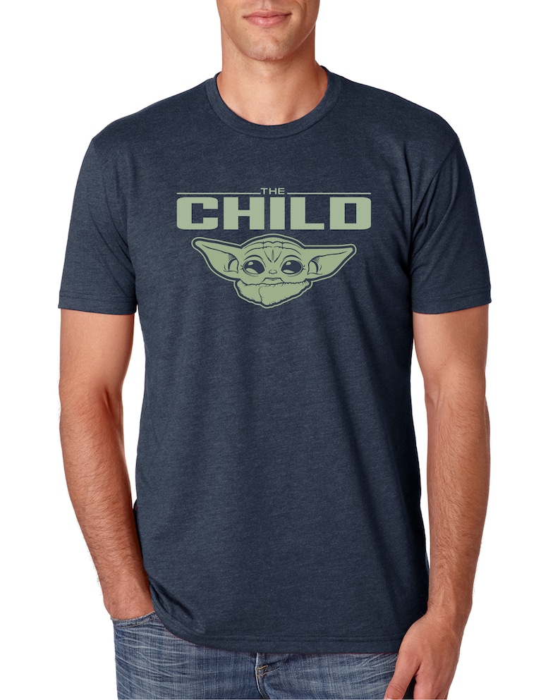 May include: Navy blue t-shirt featuring a green graphic of "The Child" from the Star Wars series. The text "THE CHILD" is above the character's image. The shirt is short-sleeved and made of a soft material.