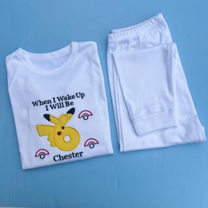 May include: White pyjama set with a yellow Pikachu design, black accents, and the text "When I Wake Up I Will Be Chester". The set includes a long-sleeved top and matching trousers.
