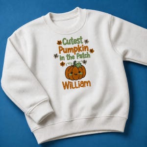 May include: A white long-sleeve sweatshirt featuring an embroidered design with the text Cutest Pumpkin in the Patch and the name William. The design includes a smiling orange pumpkin graphic surrounded by small brown and green autumn leaves.