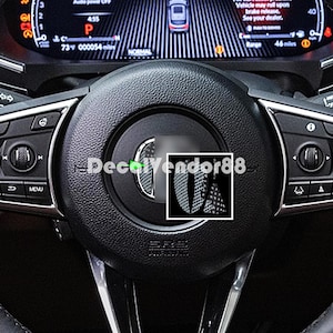 May include: A black steering wheel with a carbon fiber trim and a green LED light. The steering wheel has a silver trim around the edge and a silver button on the left side. The text "DecalVendor88" is visible on the trim.