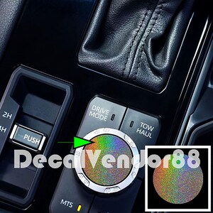 May include: Close-up of a car's interior console featuring a multi-colored, iridescent control knob with a silver trim. The console includes buttons labeled "DRIVE MODE" and "TOW HAUL". The text "DecalVendor88" is overlaid on the image.
