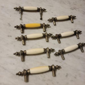 Puede incluir: Un juego de ocho pomos de armario vintage con acabado de cerámica blanca y herrajes de latón antiguo. Los pomos tienen un diseño simple y elegante y serían una gran adición a cualquier cocina o baño.