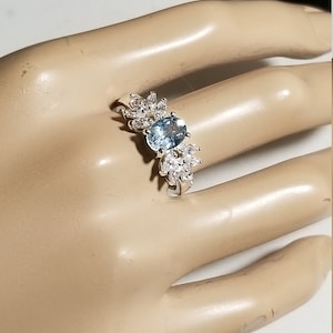 May include: A silver ring featuring a light blue oval gemstone surrounded by smaller clear gemstones.