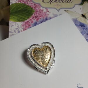 May include: A silver heart-shaped pendant with a gold heart inside. The gold heart has a swirl pattern.