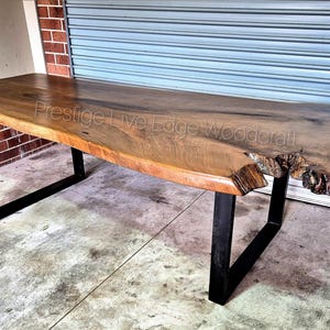 May include: A large, live edge wooden table with a natural wood finish and black metal legs. The table has a unique, irregular shape and is perfect for a modern dining room or living room.