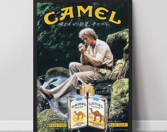 May include: Framed vintage Camel cigarettes advertisement. The poster features a man sitting on a rock, lighting a cigarette. Two packs of Camel cigarettes are in the foreground. The word "CAMEL" is in yellow, with Japanese text above.