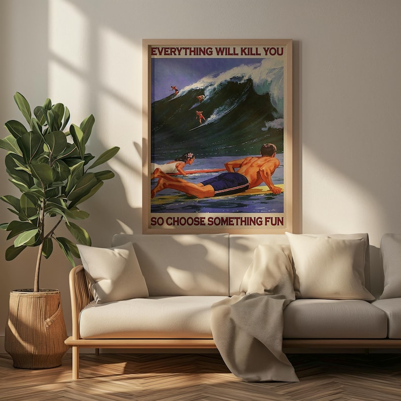 May include: A framed poster with a vintage surfing theme. The poster features a large wave with surfers and the text "EVERYTHING WILL KILL YOU SO CHOOSE SOMETHING FUN". The poster is displayed above a light-colored sofa.