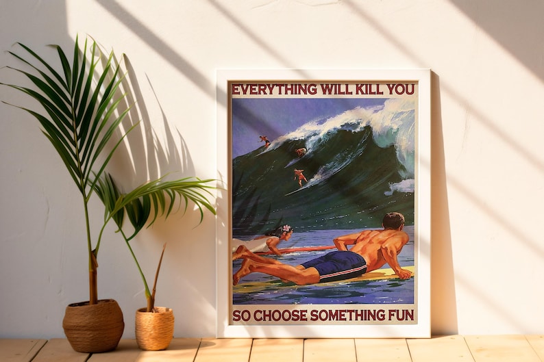 May include: Framed poster with the text "EVERYTHING WILL KILL YOU SO CHOOSE SOMETHING FUN." The image depicts surfers riding a large wave. Two people are on surfboards in the water. A palm plant is to the left of the poster.