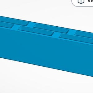 May include: A bright blue rectangular block featuring three elongated recessed slots along the top surface and a single small circular hole positioned at one end. The object has a solid, uniform construction with clean, sharp edges and a smooth finish.