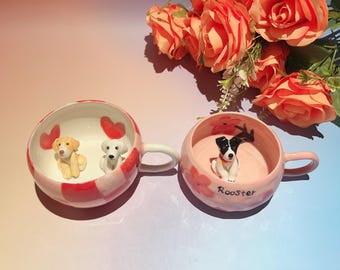 Può includere: Due tazze in ceramica con figurine di cani all'interno. Una tazza è rosa con un motivo a scacchi rossi e bianchi e dettagli a cuore rossi. L'altra è rosa con dettagli floreali e la parola "Rooster". Un mazzo di rose arancioni sullo sfondo.