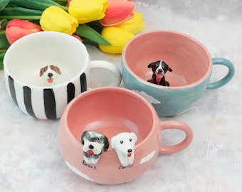 May include: Three ceramic mugs with dog figurines inside. One mug is white with black stripes, another is light blue, and the third is pink. The pink mug has two dog figurines and the names "Beans" and "Conner" written on it.
