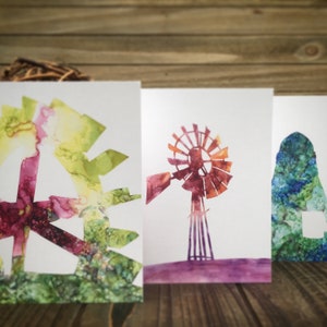 May include: Three watercolor paintings on white cardstock. The first painting is a green, yellow, and purple abstract design. The second painting is a red and orange windmill with a purple base. The third painting is a blue and green abstract design.