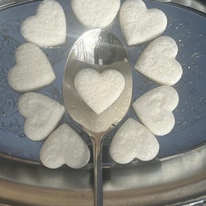May include: A silver serving tray with a silver spoon and nine white heart-shaped sugar cubes.