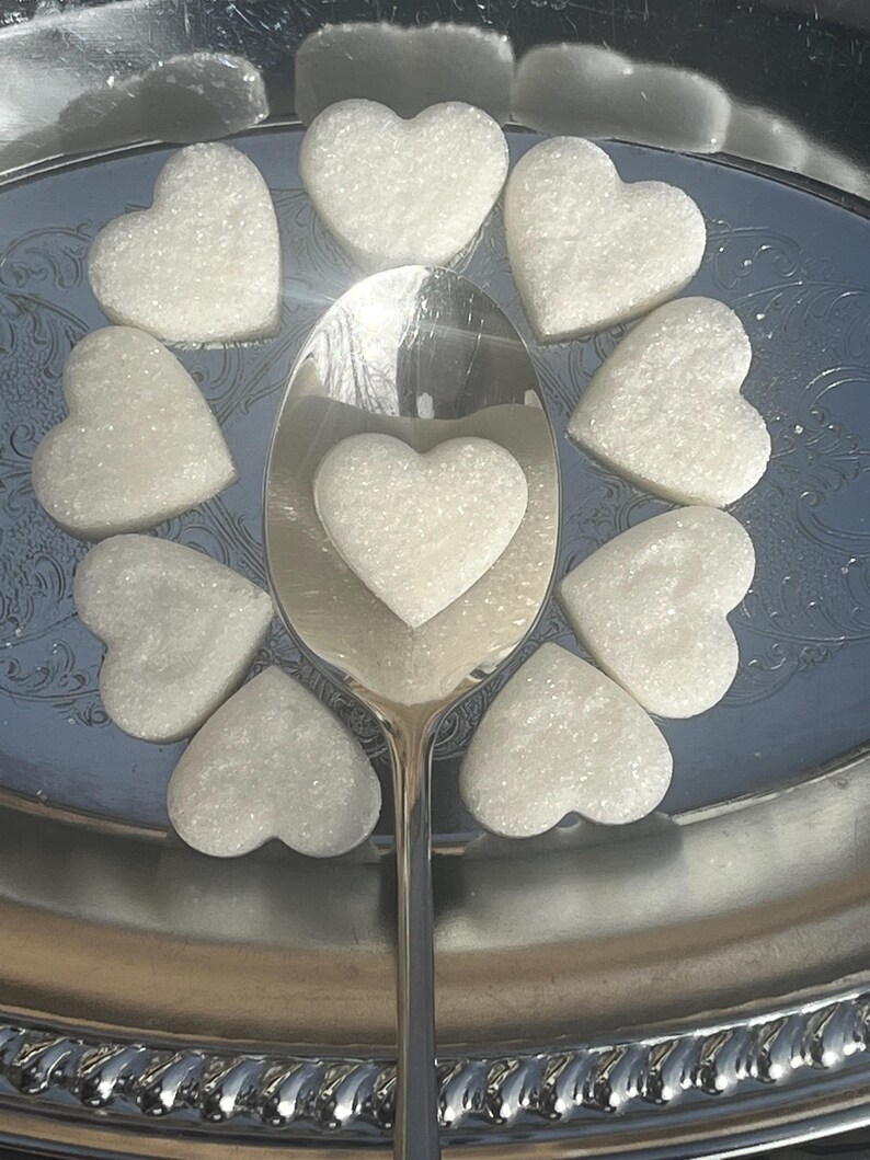 May include: A silver serving tray with a silver spoon and nine white heart-shaped sugar cubes.