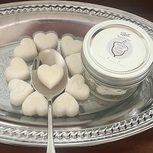 May include: A silver tray with a glass jar of white sugar cubes. The jar has a label that reads "Ball SureTight Acorn Cap Sugar Cubes". The tray is filled with heart-shaped sugar cubes.