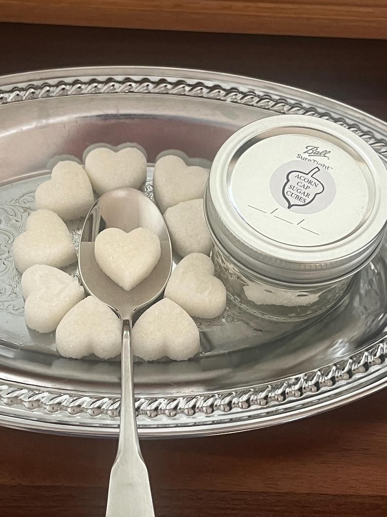 May include: A silver tray with a glass jar of white sugar cubes. The jar has a label that reads "Ball SureTight Acorn Cap Sugar Cubes". The tray is filled with heart-shaped sugar cubes.