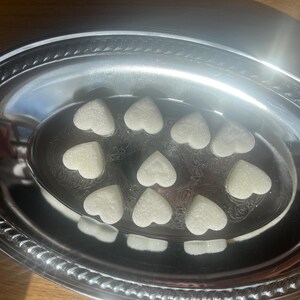 May include: A silver oval serving dish with a decorative border holds 10 white heart-shaped sugar cubes.