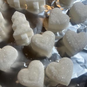 May include: A collection of white sugar cubes shaped like hearts and Christmas trees on a silver foil surface.