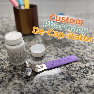 Puede incluir: Un frasco de pastillas blanco con una tapa blanca y una herramienta "DECAPITATOR" morada. La herramienta es de metal y tiene un extremo curvado. El texto "Custom Pharmacy De-Cap-itator!" está en el fondo.