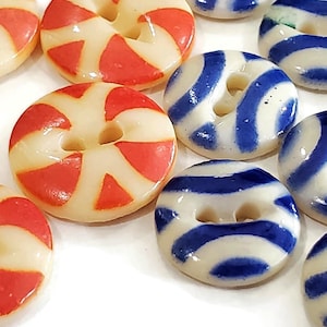 Peut inclure: Gros plan de plusieurs boutons ronds à deux trous. Certains boutons ont une base crème avec des rayures rouges, tandis que d'autres ont une base crème avec des rayures bleues. Les boutons sont brillants.