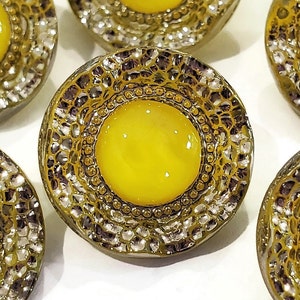 Closeup photo of a 1950s moon glow glass button with a bright yellow center surrounded by sparkly silver luster.