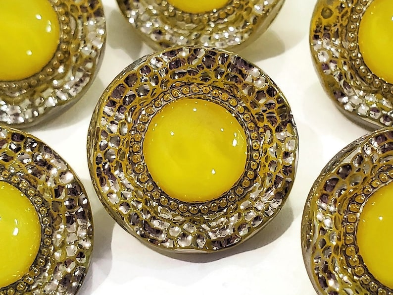 Closeup photo of a 1950s moon glow glass button with a bright yellow center surrounded by sparkly silver luster.