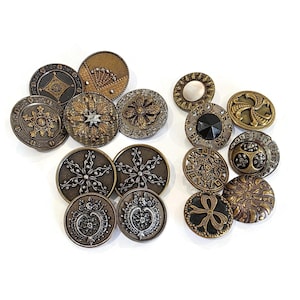 May include: A collection of round metal buttons featuring various embossed designs, including floral patterns, geometric shapes, starbursts, and a bow motif. The buttons display metallic finishes in shades of antique gold, bronze, and dark silver.