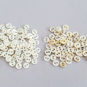 May include: A large pile of white and cream colored two-hole buttons. The buttons are made of a pearlescent material.