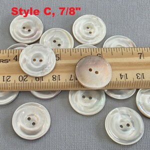 May include: A collection of round, pearlescent buttons with two holes each. The buttons are approximately 7/8 inch in diameter. The text "Style C, 7/8"" is visible in the upper left corner. A wooden ruler is used to measure the buttons.