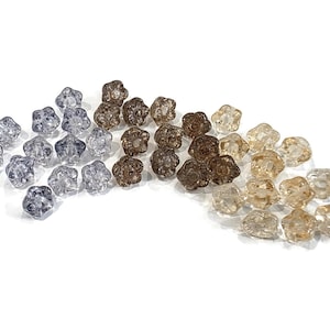 May include: A collection of small, translucent, flower-shaped beads arranged in a gradient color pattern. The beads transition from clear and light gray on the left, to medium brown in the center, and light beige or champagne on the right side.
