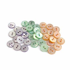 May include: A collection of round buttons in various colors, including iridescent, green, and peach. Each button has two holes for sewing. The buttons are scattered on a white background.