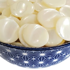 Puede incluir: Un bol lleno de botones redondos de concha nacarada blanca. El bol es azul con un patrón de estrella blanca.