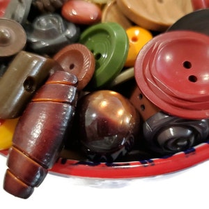 May include: A bowl filled with a variety of vintage buttons in different colors, shapes, and materials, including brown, red, green, and black.