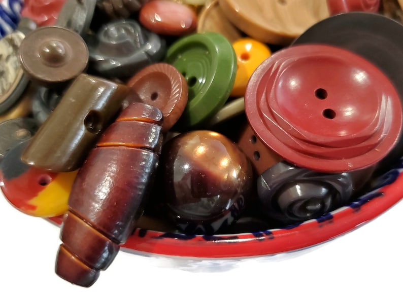 May include: A bowl filled with a variety of vintage buttons in different colors, shapes, and materials, including brown, red, green, and black.