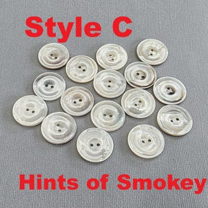 May include: A collection of round, pearlescent buttons with two holes each. The buttons have a subtle smoky hue and are arranged on a gray surface. Text in red says "Style C" and "Hints of Smokey".